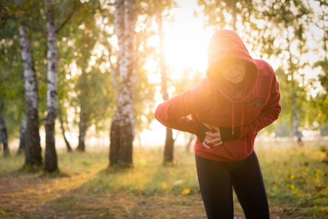Seitenstechen: Eine Joggerin stoppt den Lauf, legt die Hände in die rechte Seite und krümmt sich