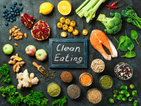 Konzept Clean Eating: Auswahl an Speisen und Zutaten umringen eine Tafel auf der mit Kreide Clean Eating steht