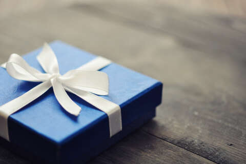 Schenken statt Erben: Eine blaue Geschenkbox mit weißem Band liegt auf einem Holztisch