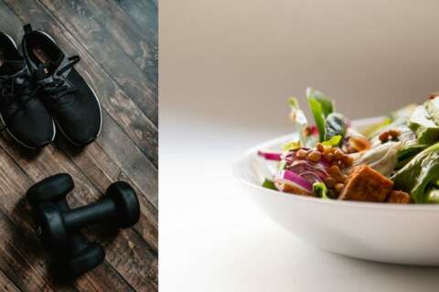 Schwarze Sportschuhe und Hanteln auf einem Holzboden und eine Schale mit Salat und Gemüse