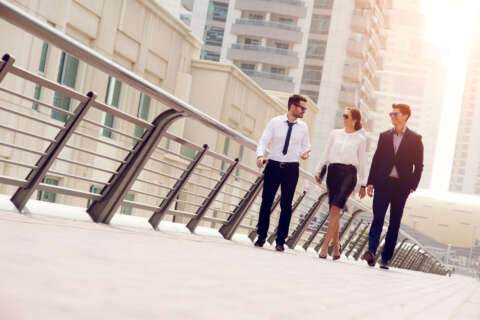 Dresscode: Eine Frau und zwei Männer im Business-Outfit laufen über eine Straße.