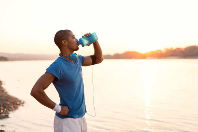 Laufplanung: Ein junger Mann stoppt am See seinen Lauf um Wasser zu trinken
