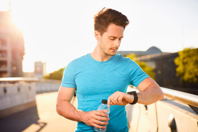 Junger m&auml;nnlicher L&auml;ufer checkt seinen Fitness-Tracker w&auml;hrend seiner Laufrunde