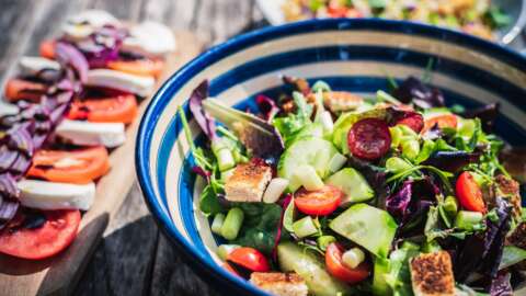 Gesunde Ernährung: Eine blau weiß gestreifte Schüssel mit Salat, daneben ein Brettchen mit Tomate und Mozzarella-Scheiben