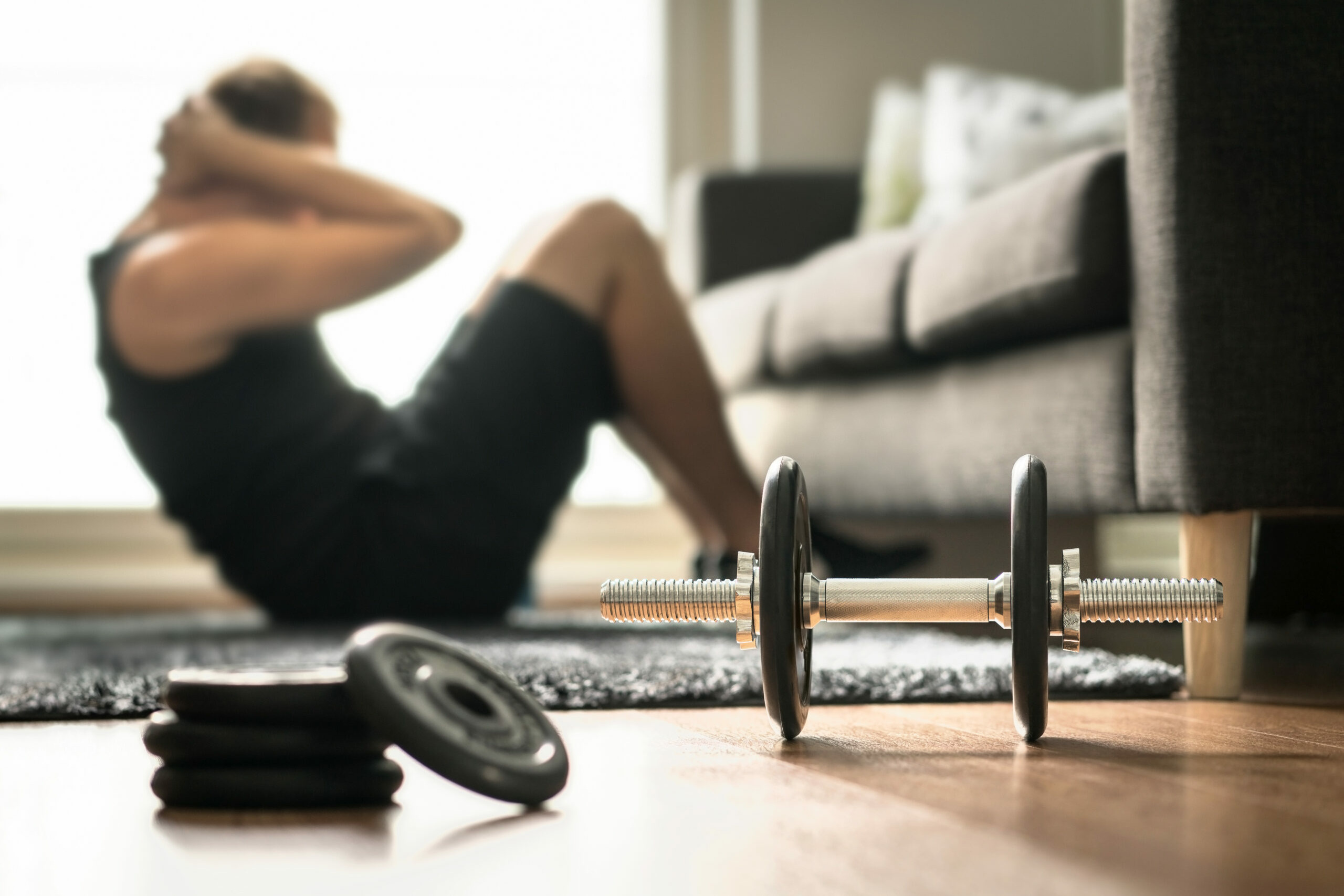 Krafttraining: Ein Mann trainiert Crunches im Wohnzimmer. Neben ihm liegt eine Hantel mit Gewichten zum Workout.
