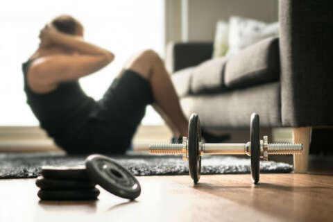 Krafttraining: Ein Mann trainiert Crunches im Wohnzimmer. Neben ihm liegt eine Hantel mit Gewichten zum Workout.