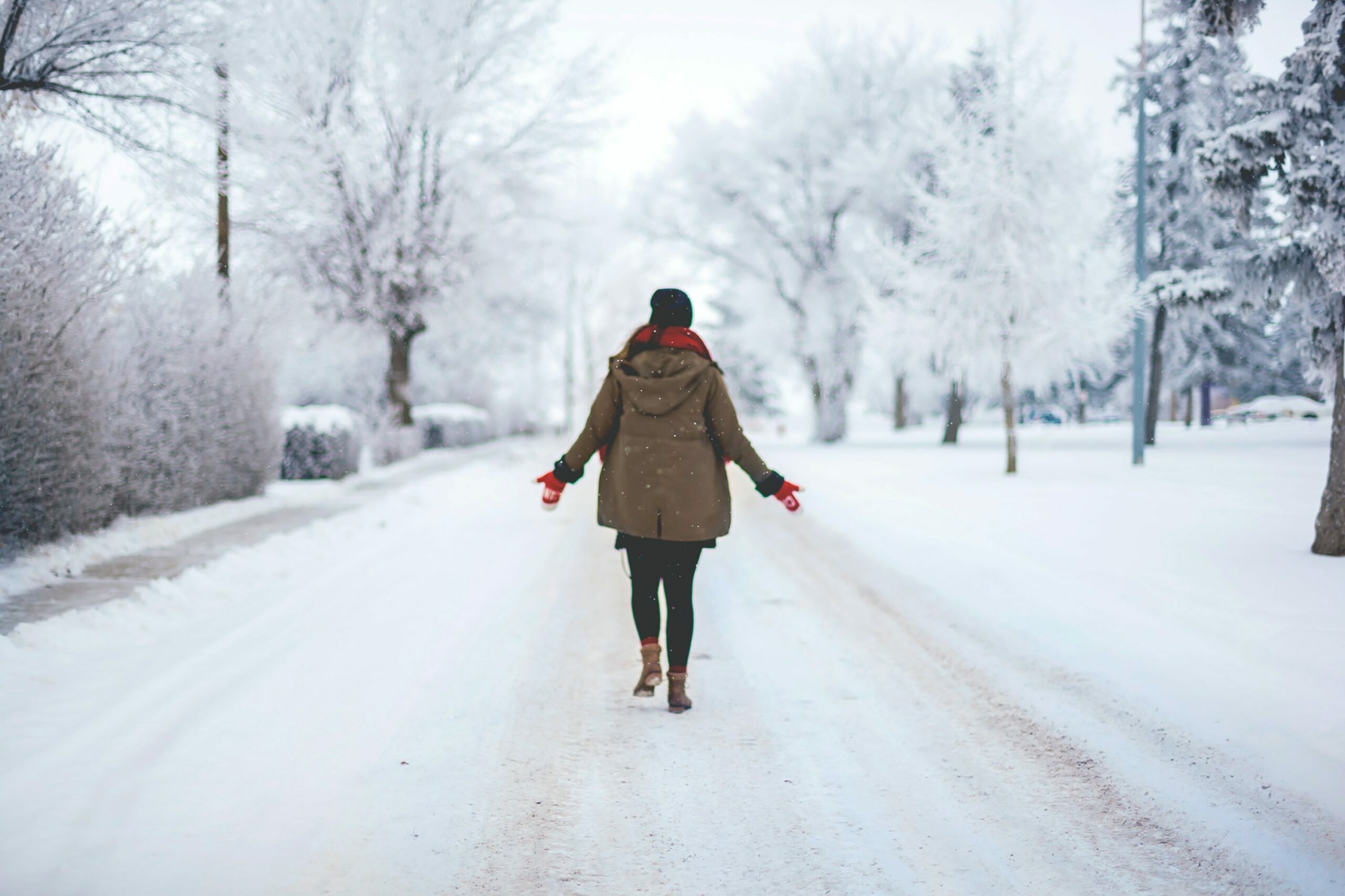 Haut: Eine Frau spaziert über eine verschneite Straße in einem Wohngebiet