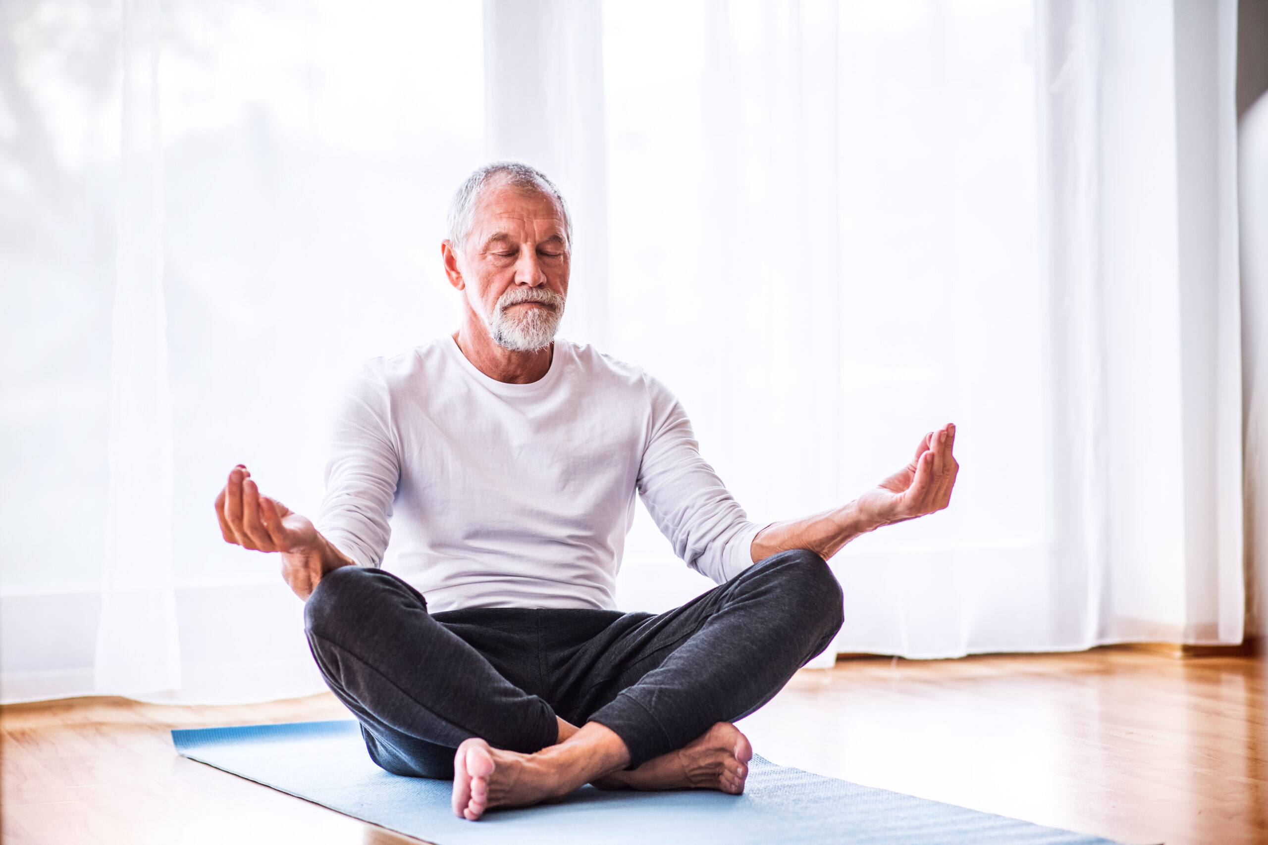Älterer Mann sitzt in einem Raum auf einer Yogamatte und meditiert
