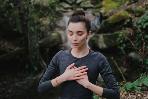 Richtig atmen: Junge Frau bei einer Atemübung vor einem Wasserfall im Wald