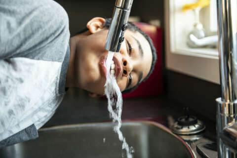 Wasser trinken: Ein Junge beugt sich in der Küche über das Spülbecken und trinkt aus dem Wasserkrahn
