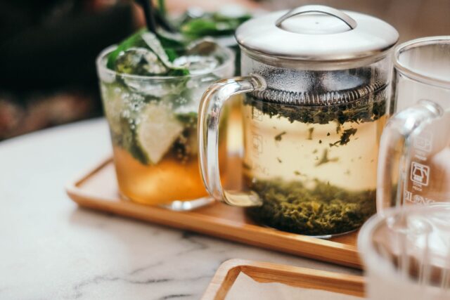 Tee: Eine Tasse Tee mit frischen Kräutern und einer Teekanne aus Glas
