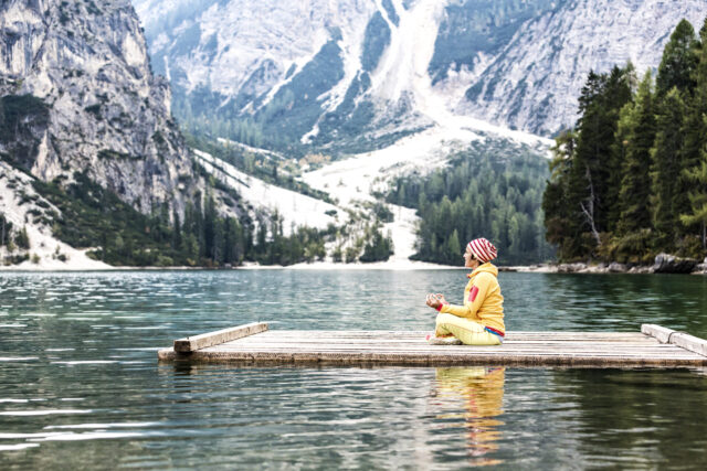 Atemübung gegen Stress: Eine Frau sitzt auf einem Seesteeg und sitz im Yoga-Schneidersitz