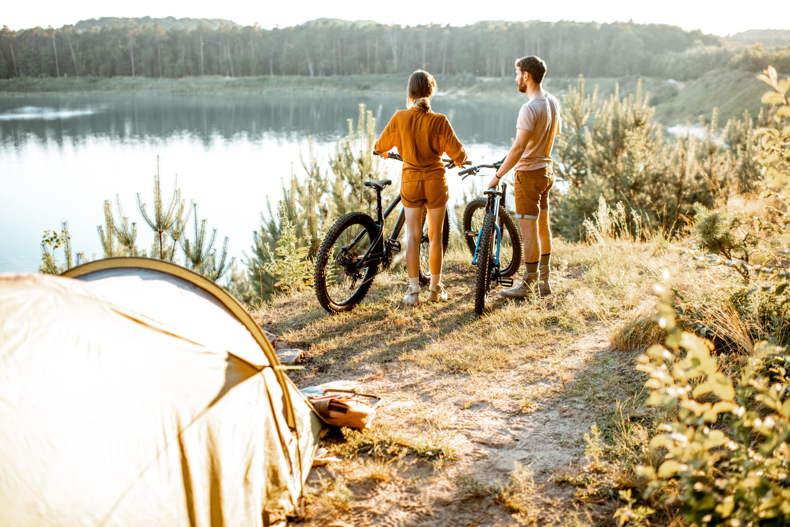 Outdoor-Typ: ein junges Paar steht mit Mountainbikes vor einem Zelt am See