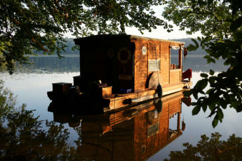 Outdoor-Typ: Hausboot aus Holz ankert an einem Seeufer im Wald