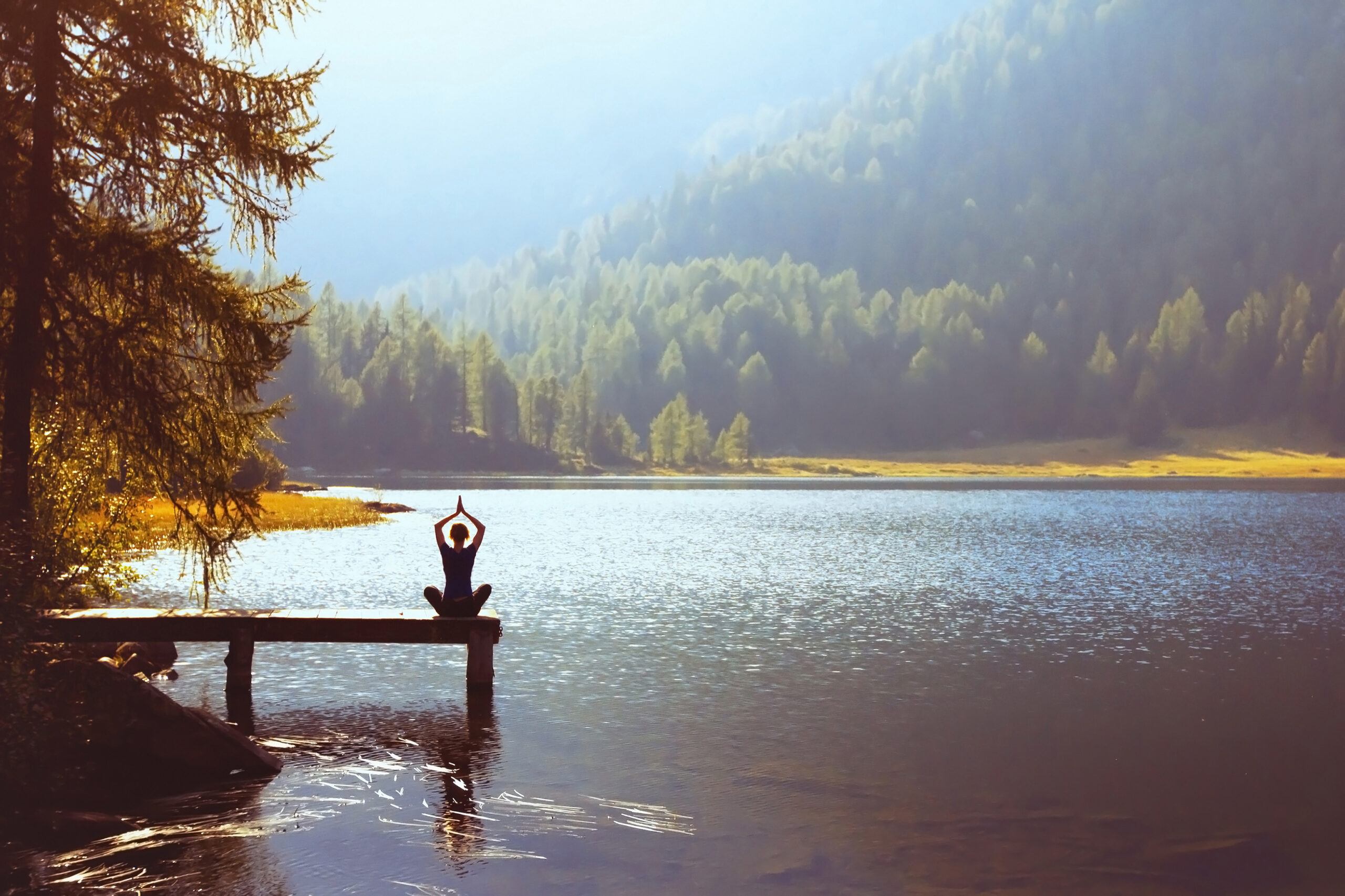 Stress: eine Frau macht Yoga auf einem Steg in einem Waldsee