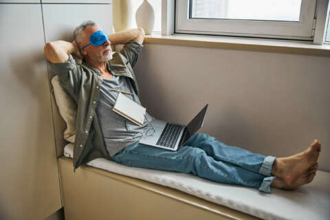 Regeneration: Mann mit Schlafmaske entspannt auf einer Sitzbank am Fenster