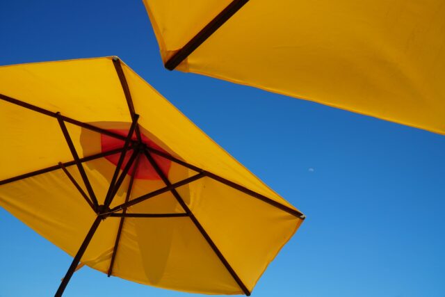 Endlich Sommer: 2 gelbe Sonnenschirme vor einem blauen Himmel