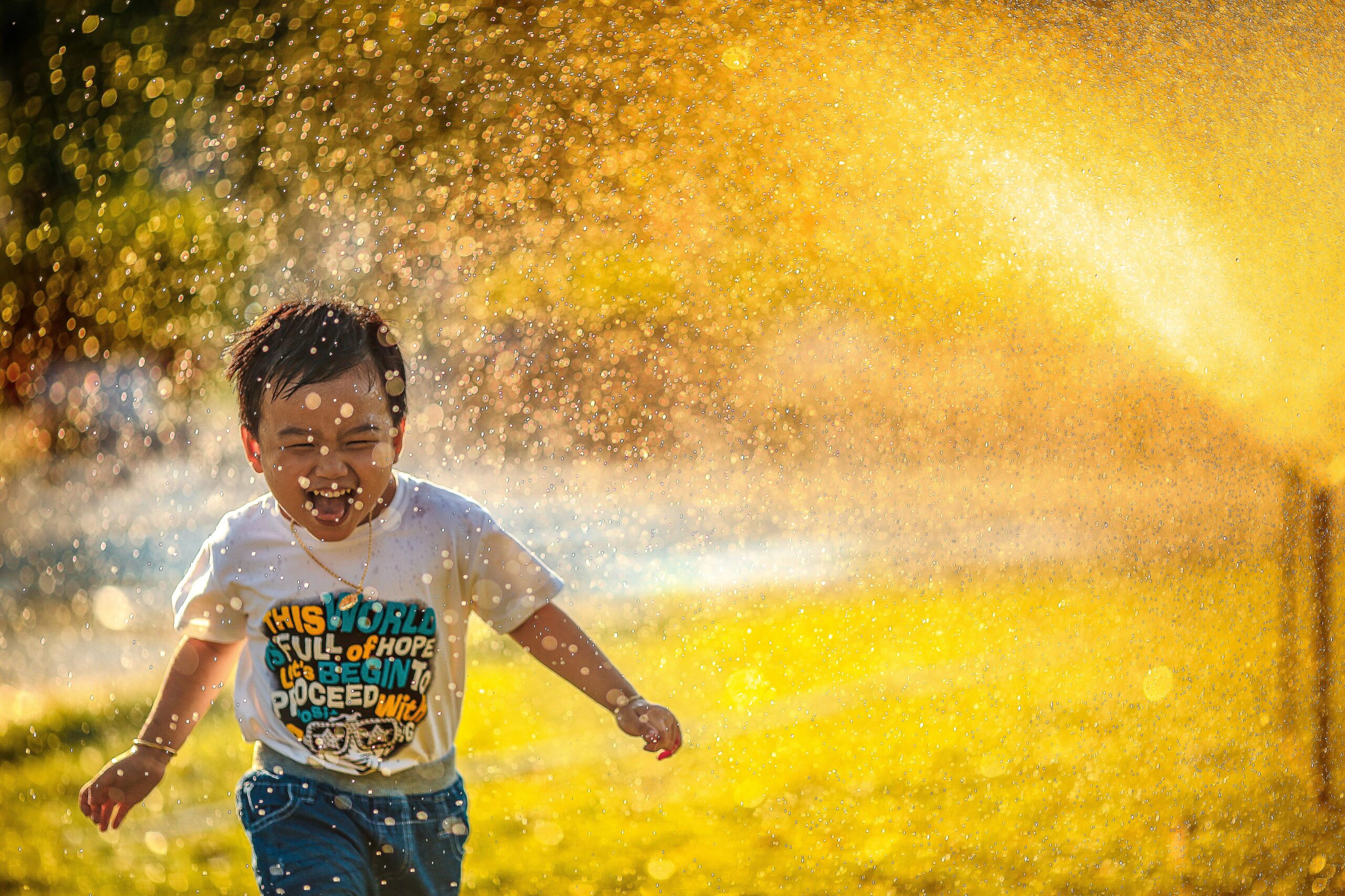 Endlich Sommer: ein kleiner Junge läuft lachend unter einem Wassersprenger hindurch