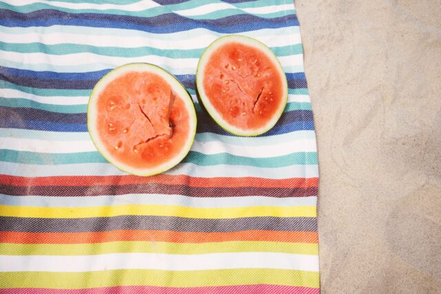 Endlich Sommer: 2 Wassermelonenhälften auf einem gestreiften Handtuch am Sandstrand