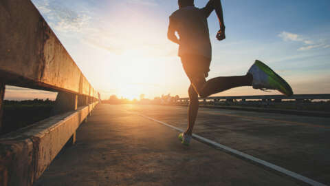 ;arathon: Mann in Sportkleidung joggt über Brücke dem Sonnenaufgang entgegen.