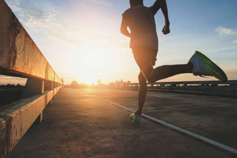 ;arathon: Mann in Sportkleidung joggt über Brücke dem Sonnenaufgang entgegen.