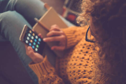 Spar dich glücklich: Frau schaut von oben auch ihr Smartphone Bildschirm und ist dabei eine App auszuwählen.