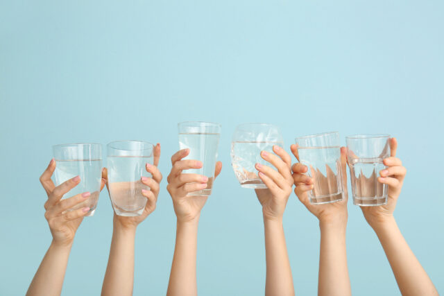 Wasser: H&auml;nde mit Wassergl&auml;sern auf blauem Hintergrund.