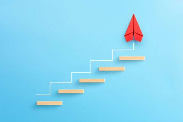 Mythen1: Wooden block stacking as step stair with red paper plane on blue background, Ladder of success in business growth concept, copy space