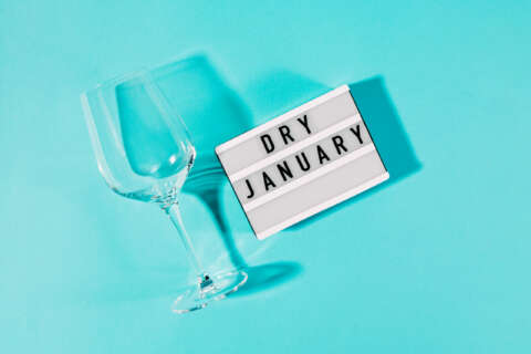 Dry January: Der Text Dry January geschrieben auf einer Lichtbox. Nebendran ein leeres Weinglas. Beides auf blauem Grund.